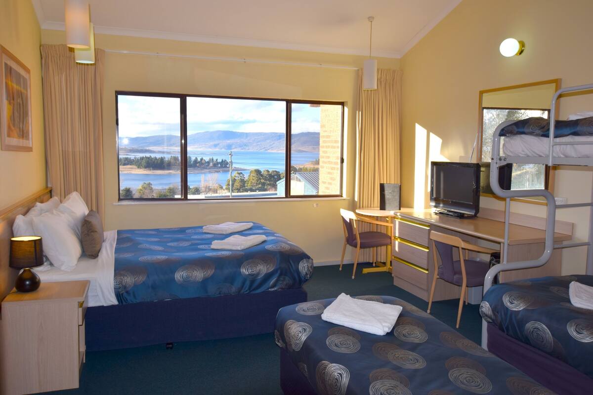 Camera d'albergo con due letti, una scrivania, una sedia, una televisione e una grande finestra vista lago e montagne.