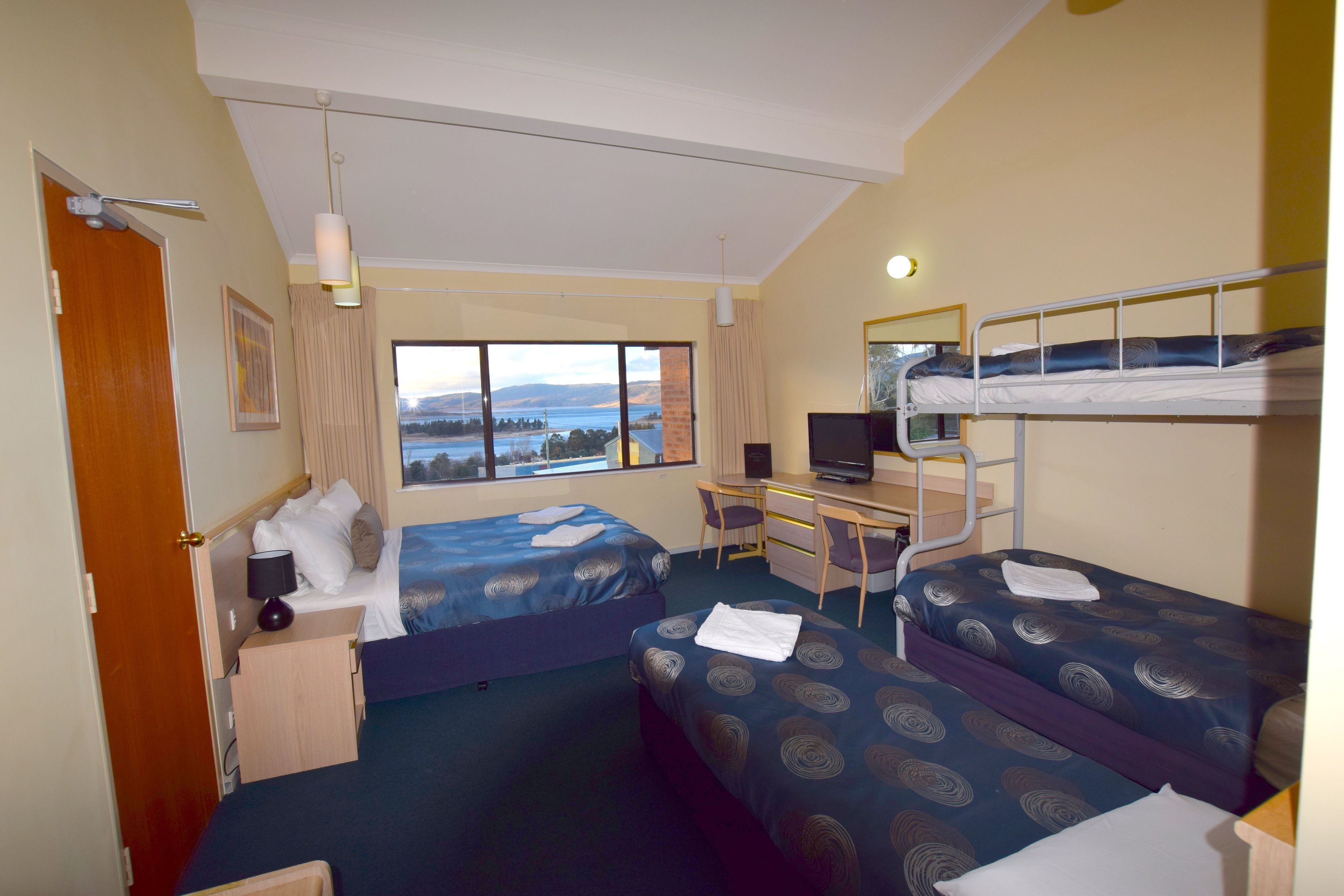 A hotel room with two beds, a desk, a TV, and a view of a lake.