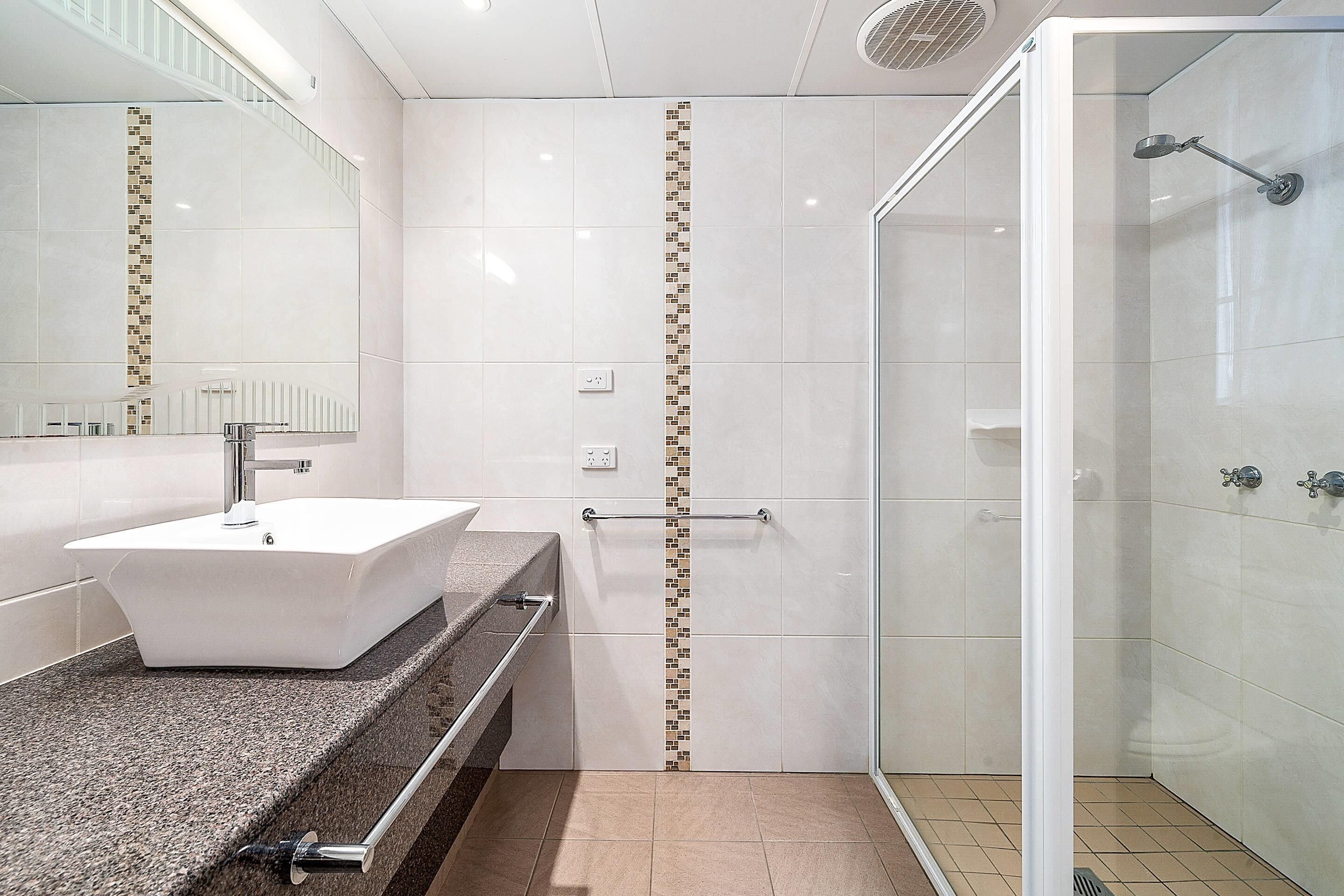 Un baño moderno con un lavabo blanco, cabina de ducha con paredes de cristal y pared revestida con zócalo decorativo.