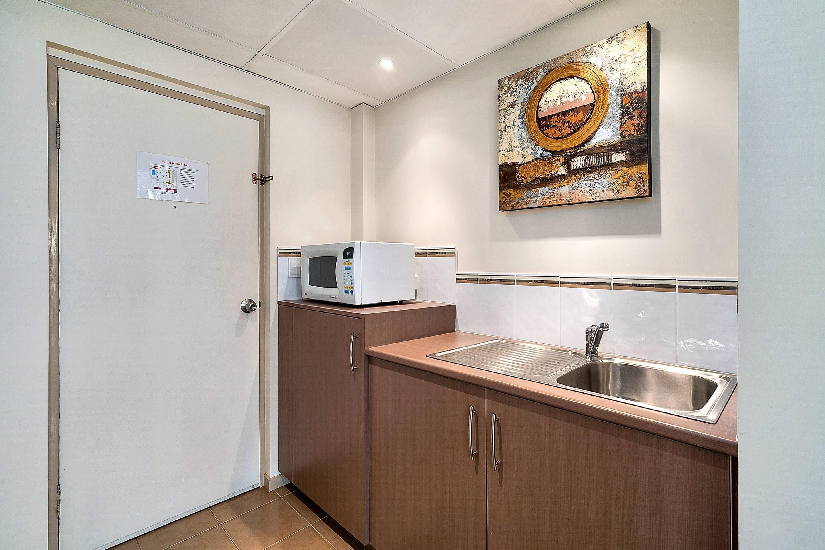 A compact kitchen with a microwave, sink, and cabinets.