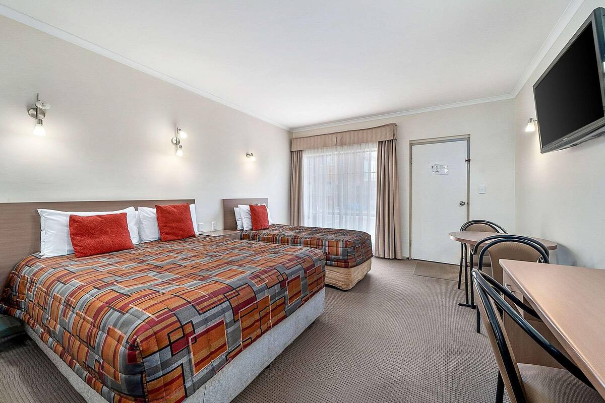 Una habitación de hotel con una cama, dos mesitas de noche, un escritorio y un televisor.