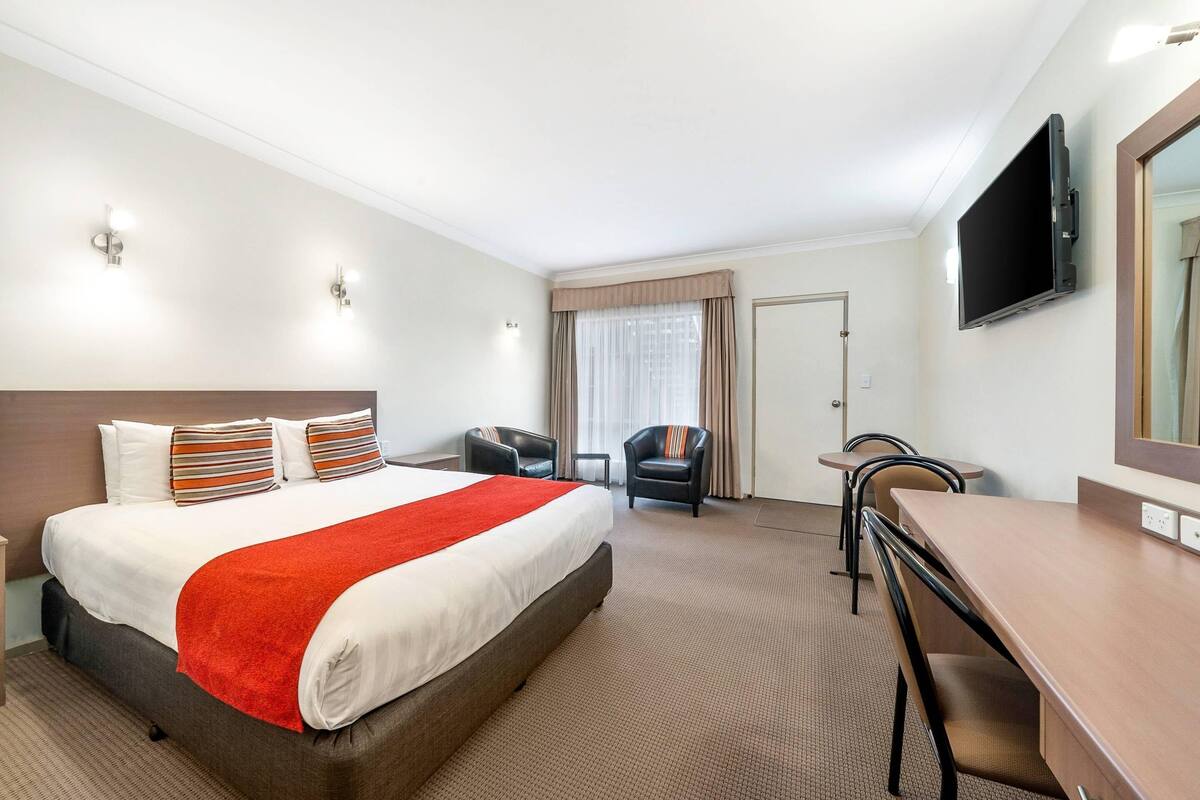 Habitación de hotel con cama, escritorio, silla, televisor y puerta.