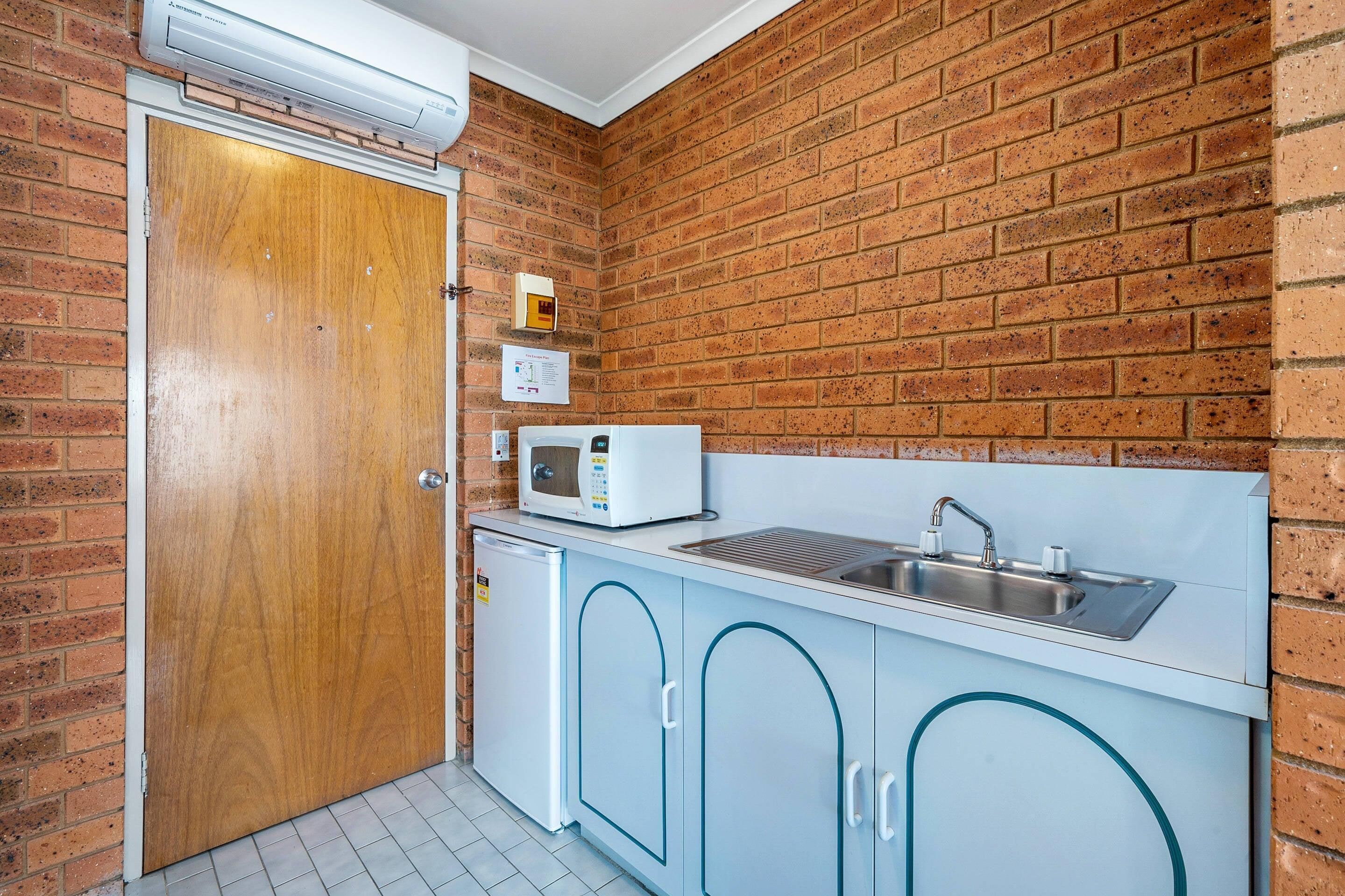 A compact kitchen with a microwave, sink, and a small refrigerator.