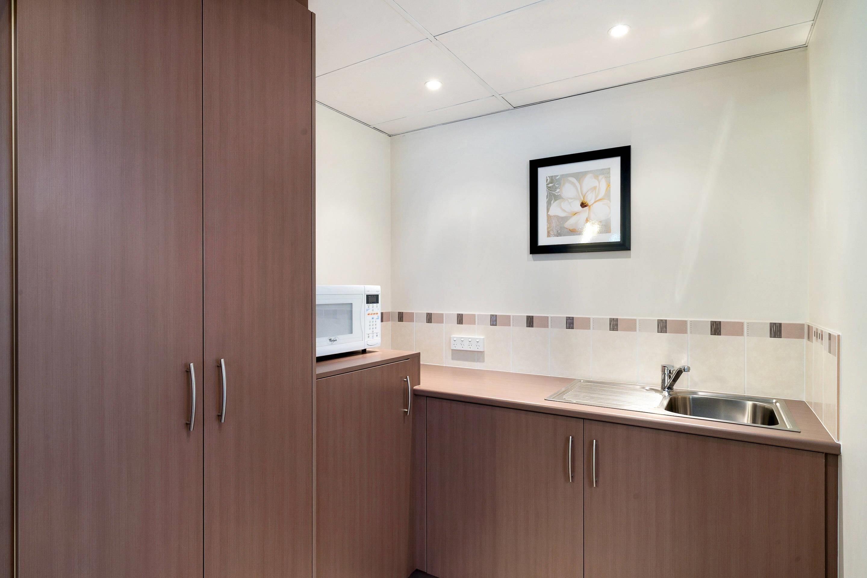 A kitchen with wooden cabinets, a microwave, a sink, and a framed picture on the wall.