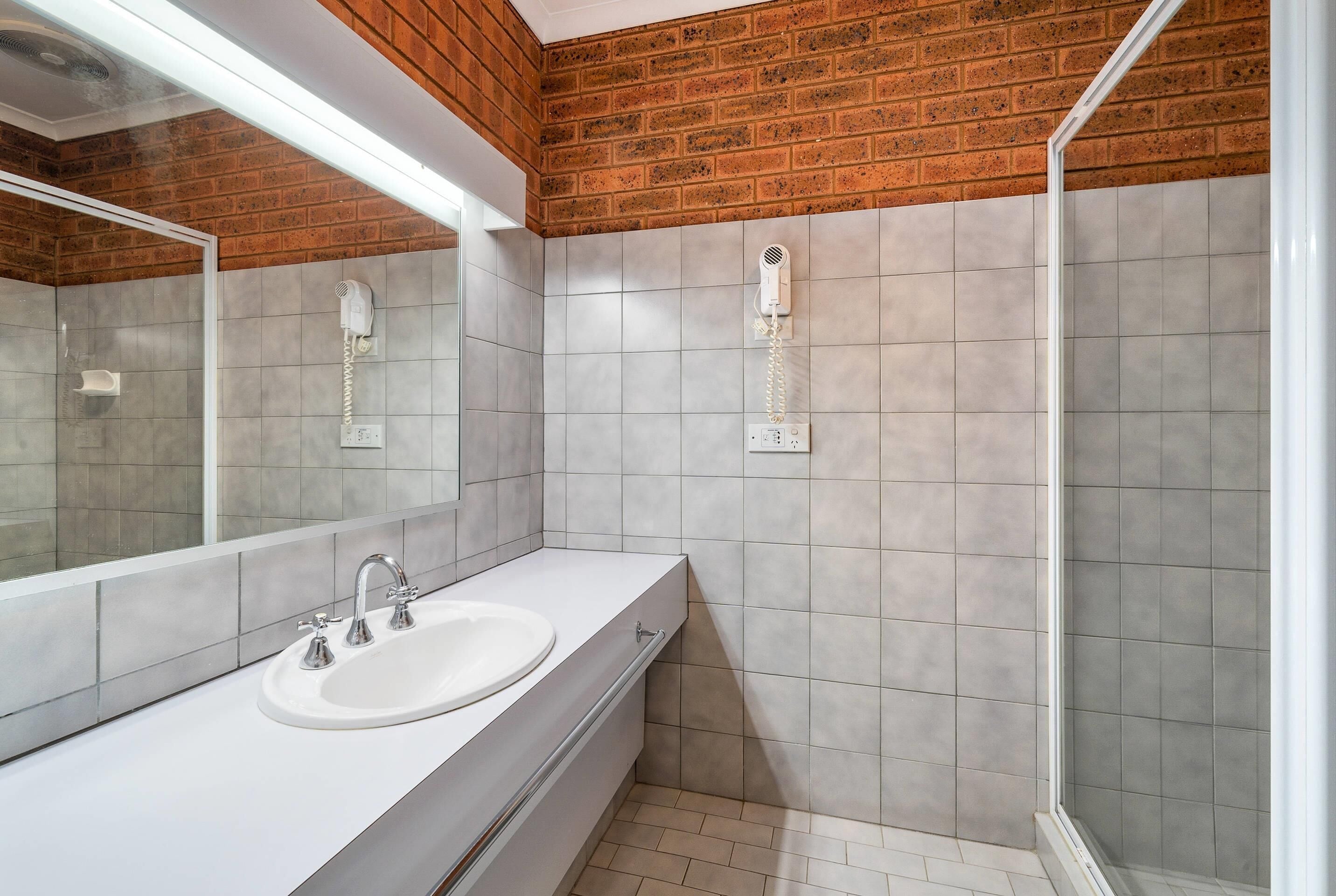 A bathroom with a white sink, a mirror, a hairdryer, and a shower area.