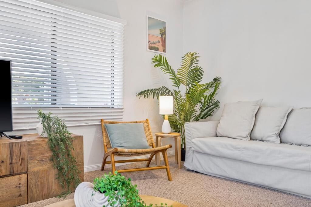 Een woonkamer met een televisie, een bank, een fauteuil, een lamp en een potplant.