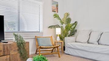 Een woonkamer met een televisie, een bank, een fauteuil, een lamp en een potplant.