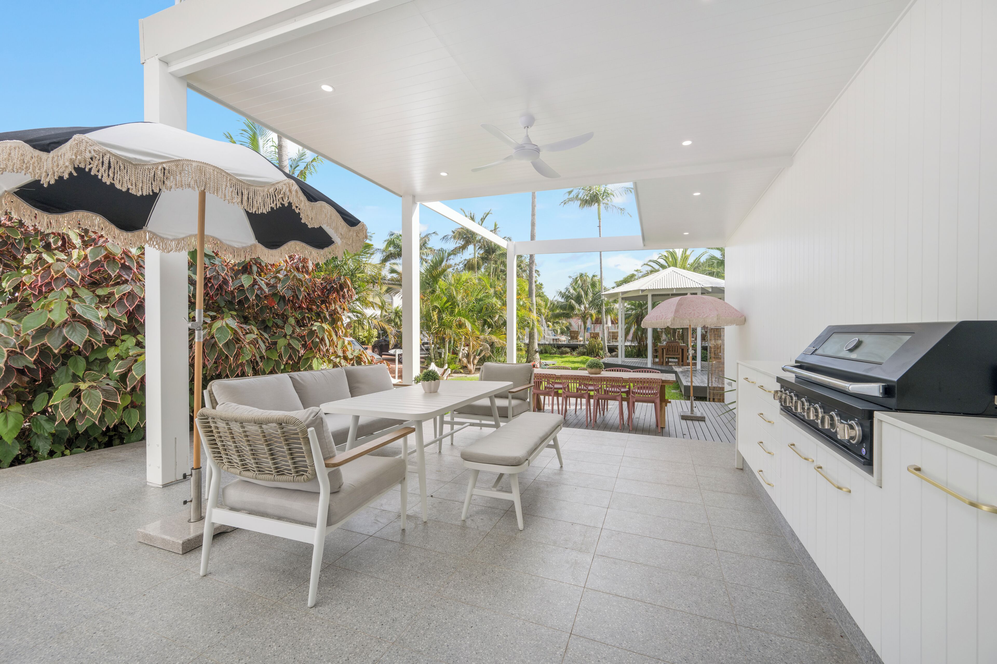 A modern outdoor patio with a dining area, a grill station, and a covered seating area with umbrellas.