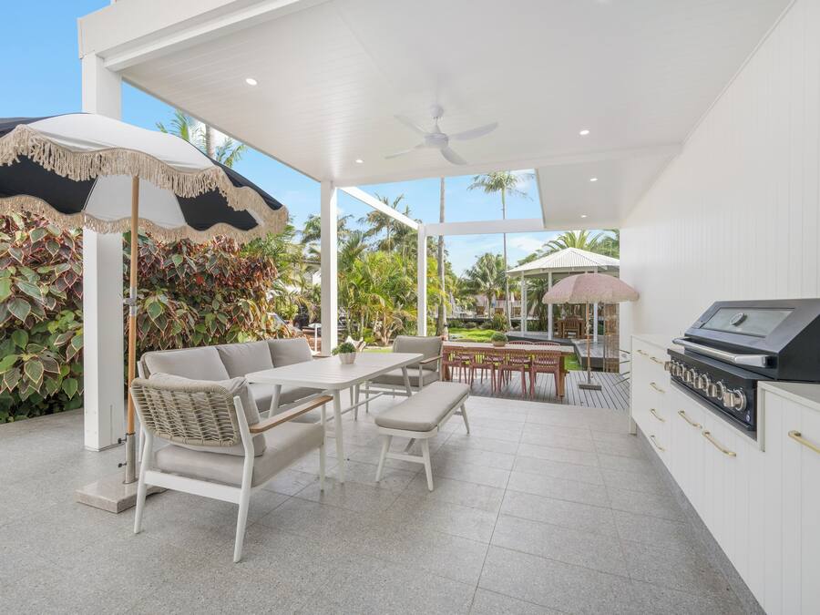 A modern outdoor patio with a dining area, a grill station, and a covered seating area with umbrellas.