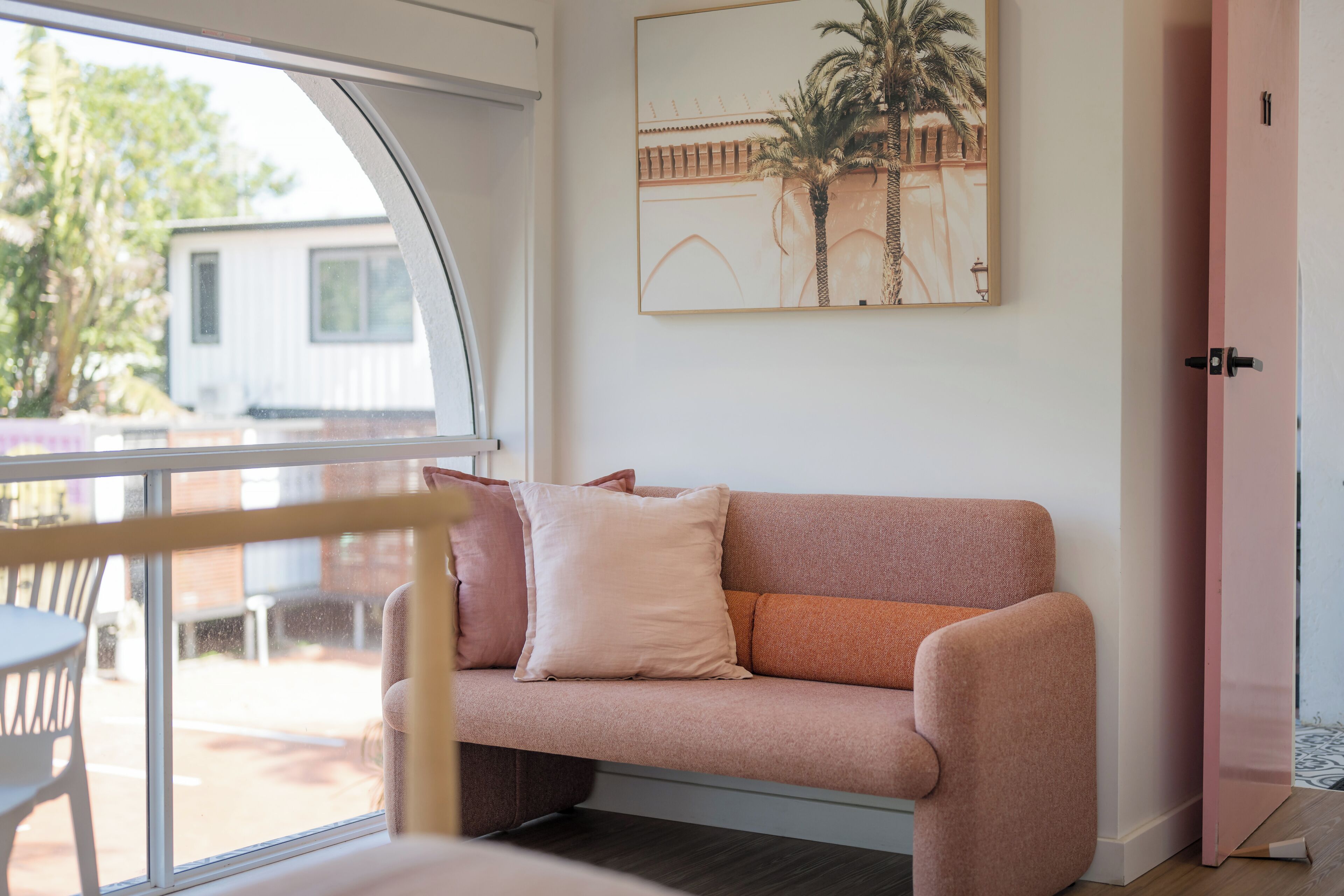Una habitación con un sofá rosa, un cuadro en la pared y una puerta a la derecha.