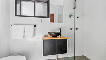 A modern bathroom with a large mirror, a black vessel sink, a white toilet, and a glass shower enclosure.
