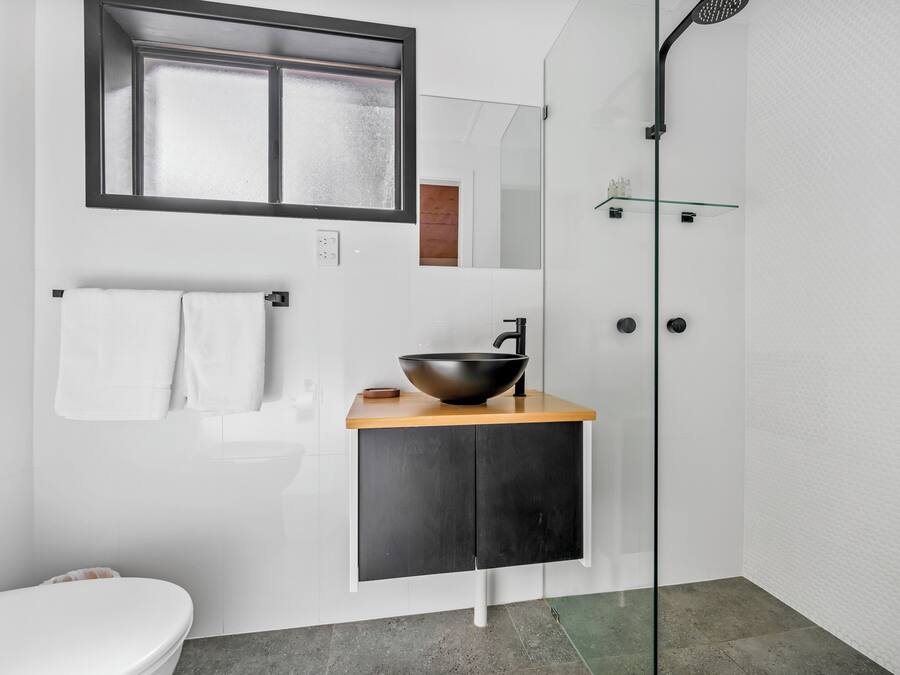 A modern bathroom with a large mirror, a black vessel sink, a white toilet, and a glass shower enclosure.