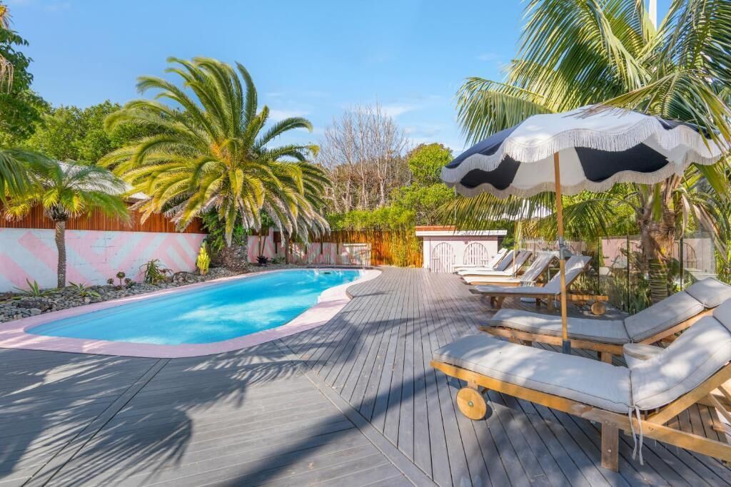 A wooden deck with a pool, lounge chairs, and palm trees.