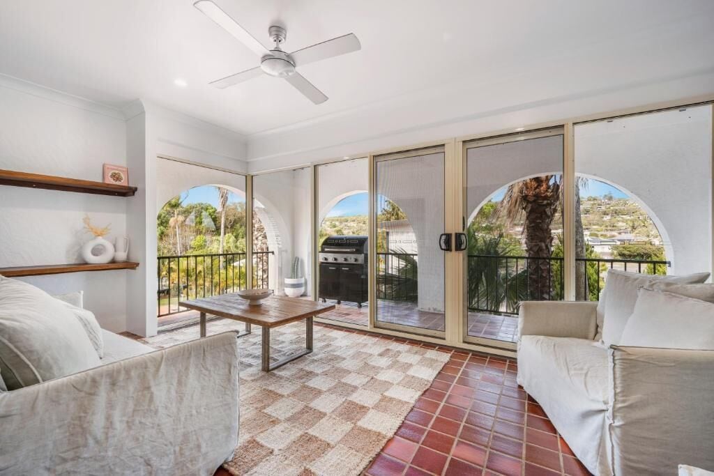 A spacious balcony with a checkered floor, a ceiling fan, and a view of the surrounding landscape.