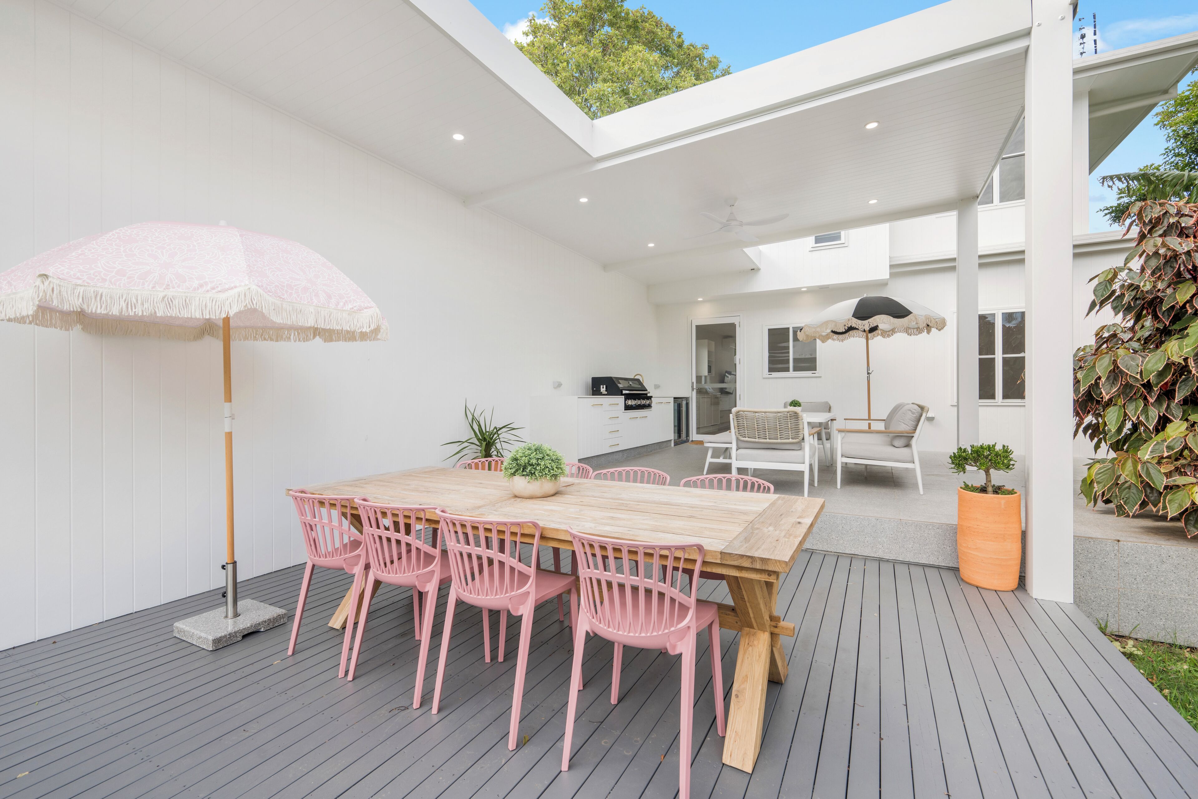 An outdoor patio with a wooden table and pink chairs, a ceiling fan, and potted plants.
