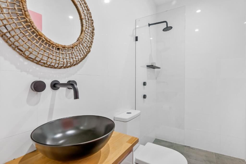 Ein modernes Badezimmer mit großem Spiegel, Holztischplatte, einem Aufsatzwaschbecken, Toilette und einer Duschkabine aus Glas.