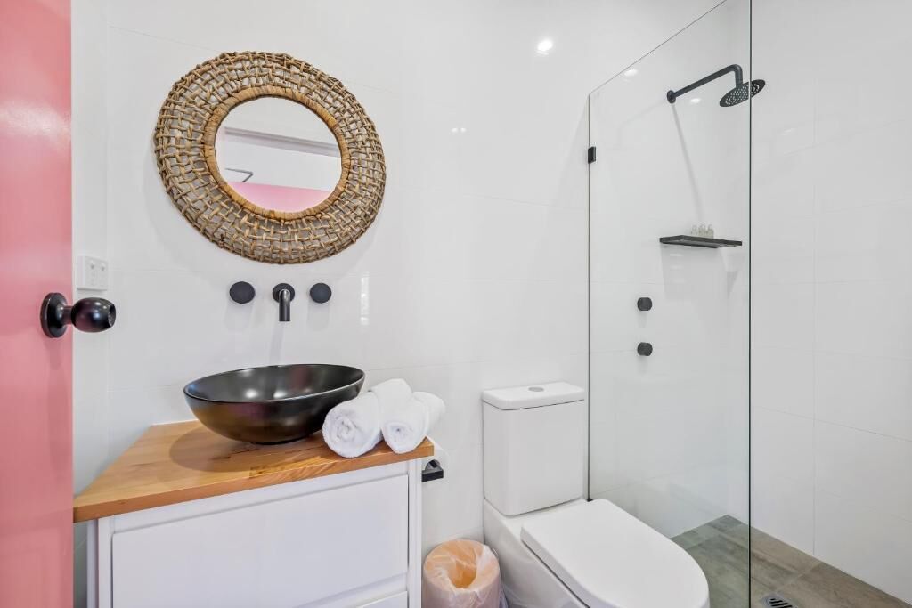 A bathroom with a round mirror, a bowl sink, a toilet, and a glass-enclosed shower.
