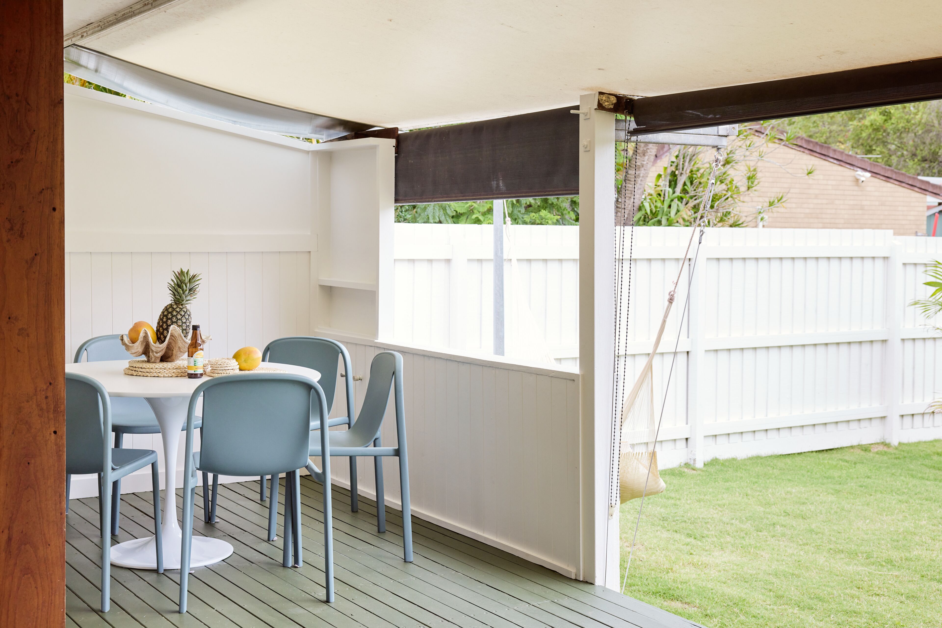 A covered patio with a table and chairs, a white fence in the background, and a hanging swing.