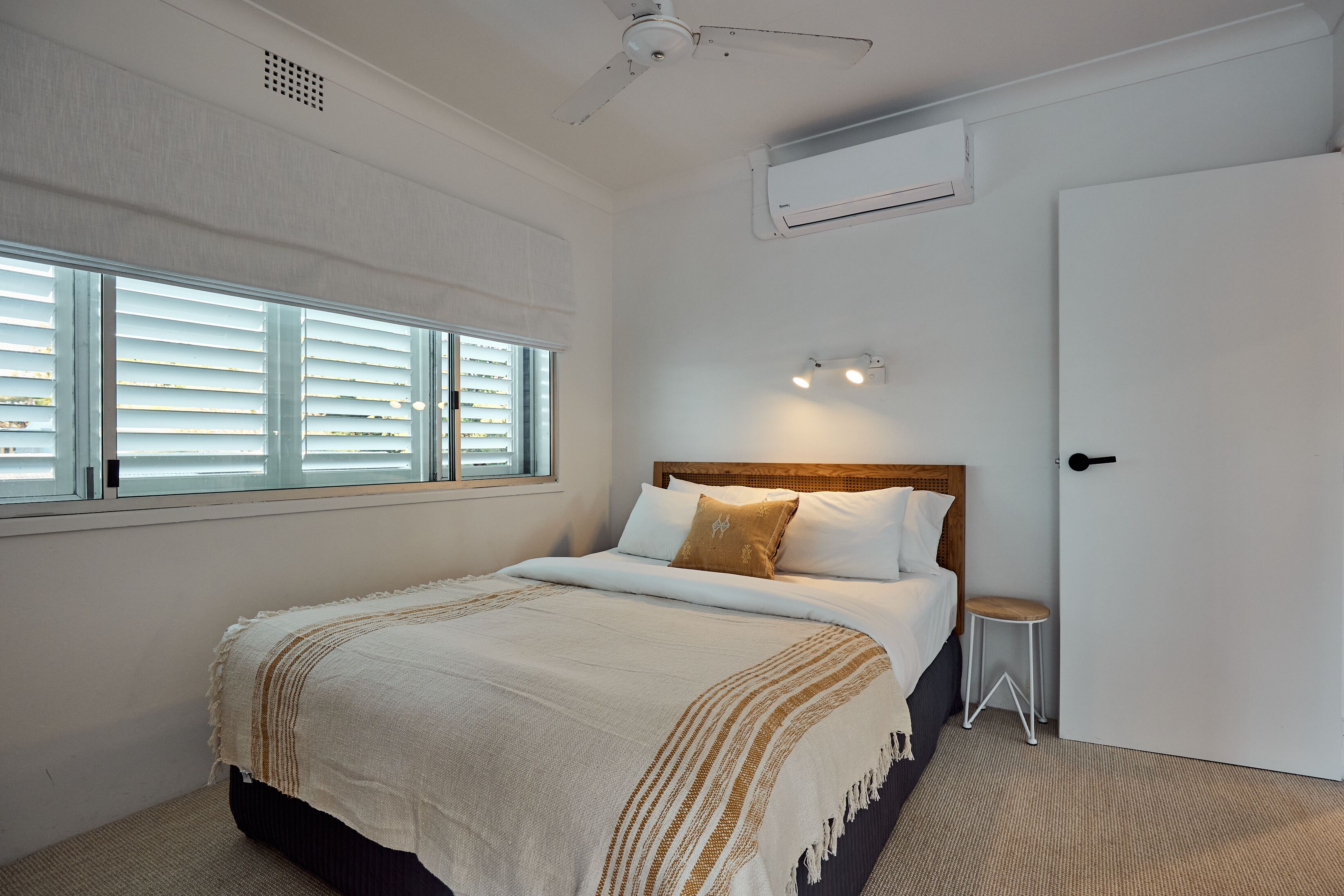 Un dormitorio con cama, ventana con persianas, ventilador de techo, aire acondicionado y puerta.