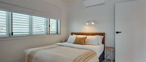 Un dormitorio con cama, ventana con persianas, ventilador de techo, aire acondicionado y puerta.