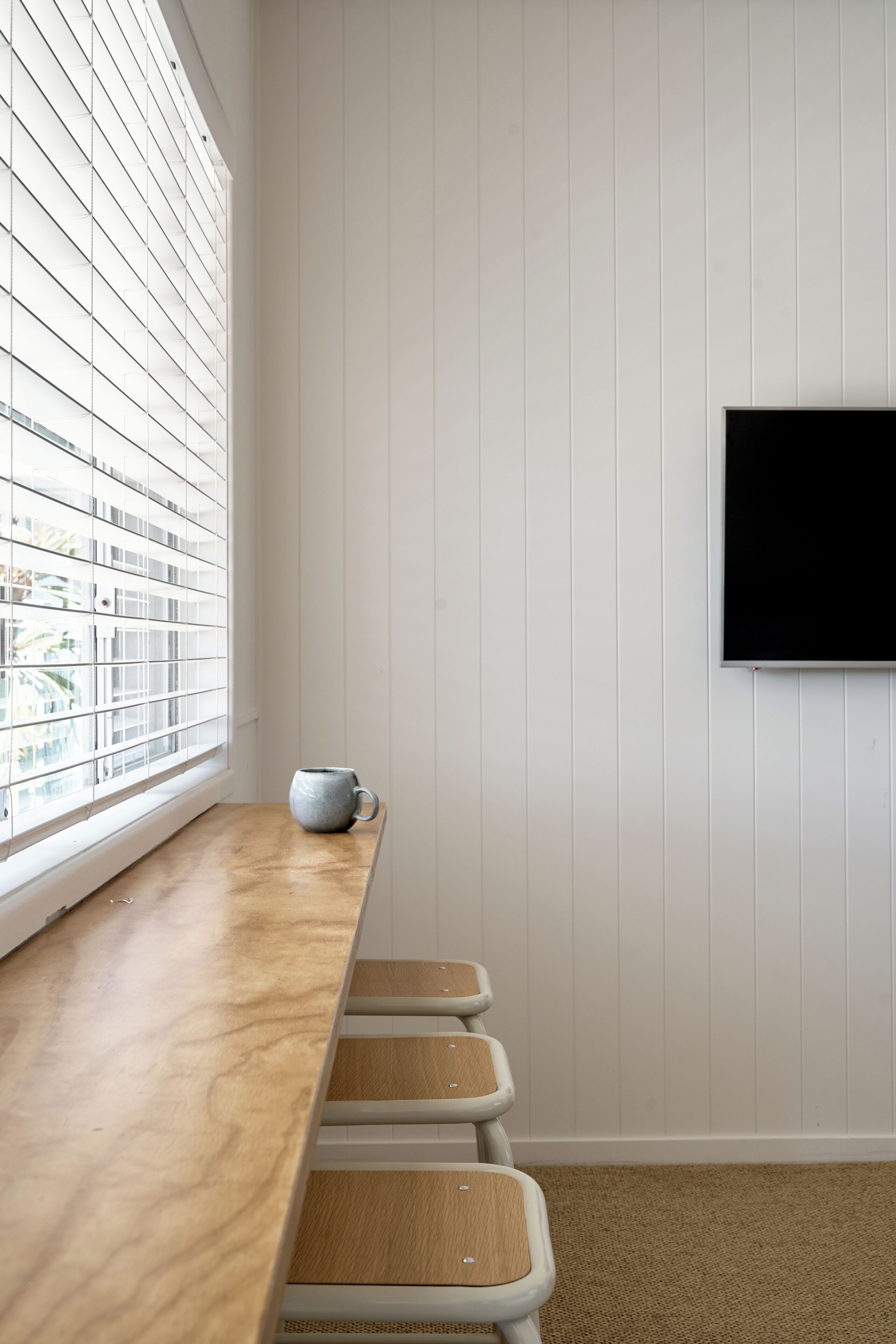 Een kamer met een houten bankje, een witte muur en een wandgemonteerde televisie.