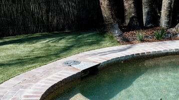 Une piscine bordée de briques et une zone herbeuse avec des arbres.