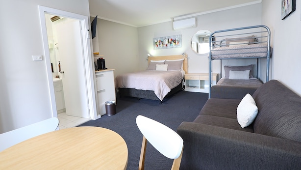 Une chambre d’hôtel compacte comprenant un lit superposé, un canapé, un bureau et une chaise.
