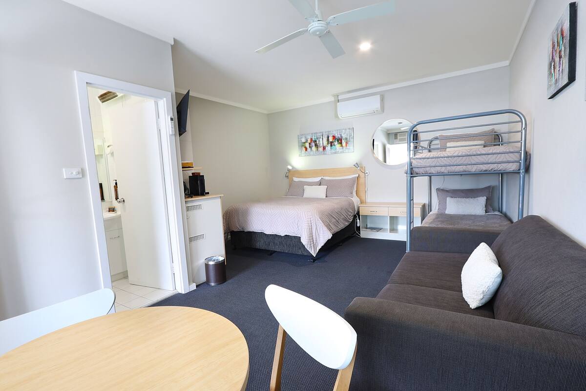 A compact hotel room with a bunk bed, a sofa, a desk, and a chair.
