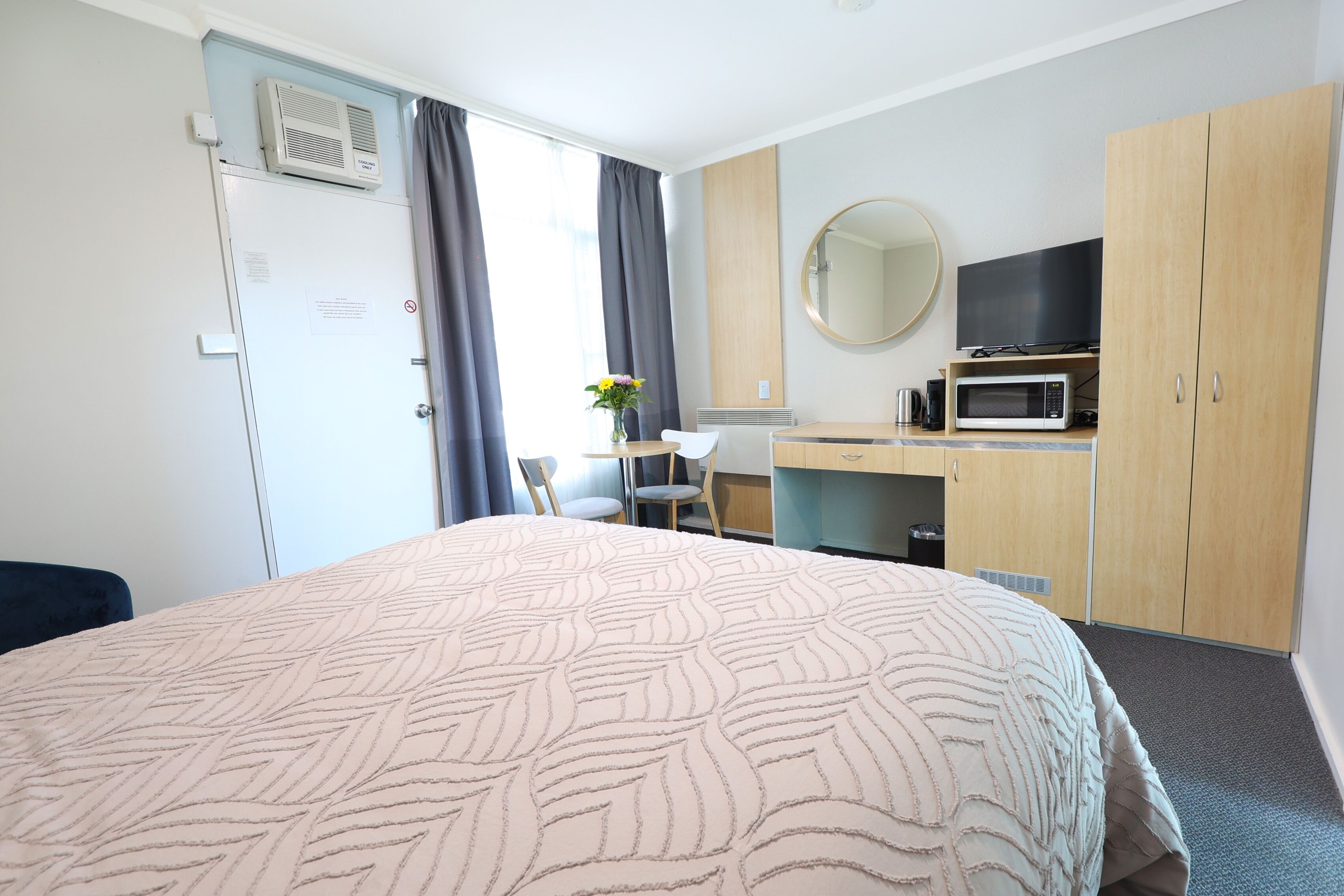 Una camera d'albergo con un letto, una scrivania, una sedia, una televisione, un forno a microonde e un armadio.