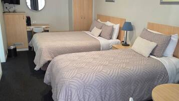 Habitación de hotel con dos camas, un escritorio, una silla, una mesita, un televisor y un armario.
