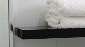 Une pile de serviettes blanches est posée sur une étagère noire dans une salle de bain.