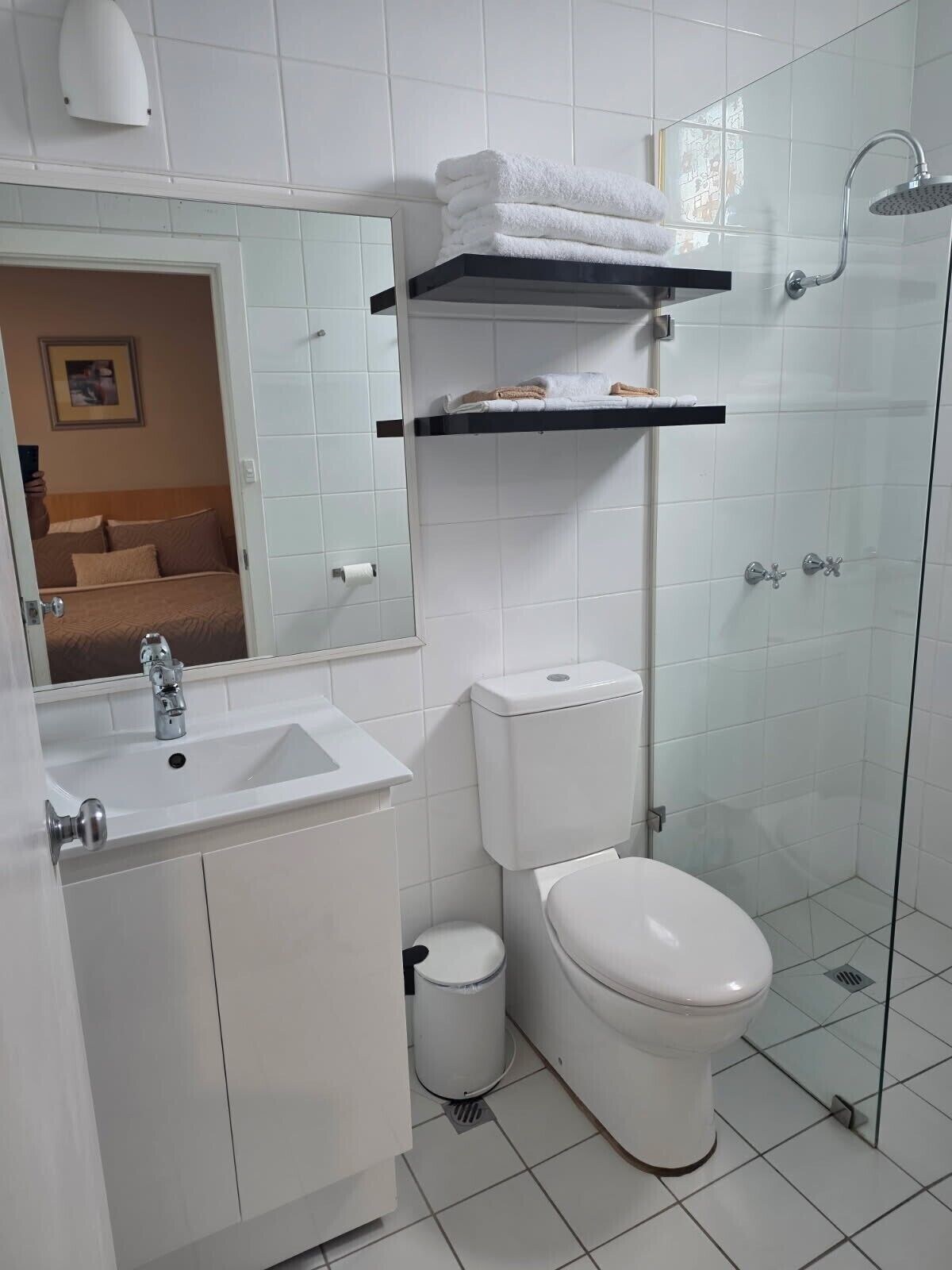 Un baño moderno con cabina de ducha de vidrio, un lavabo blanco, inodoro y espejo.
