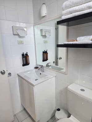 A modern bathroom with a white sink, mirror, and toilet. There are two bottles of hand soap and a towel rack with folded towels. - Nebula Motel Cooma (Cooma)