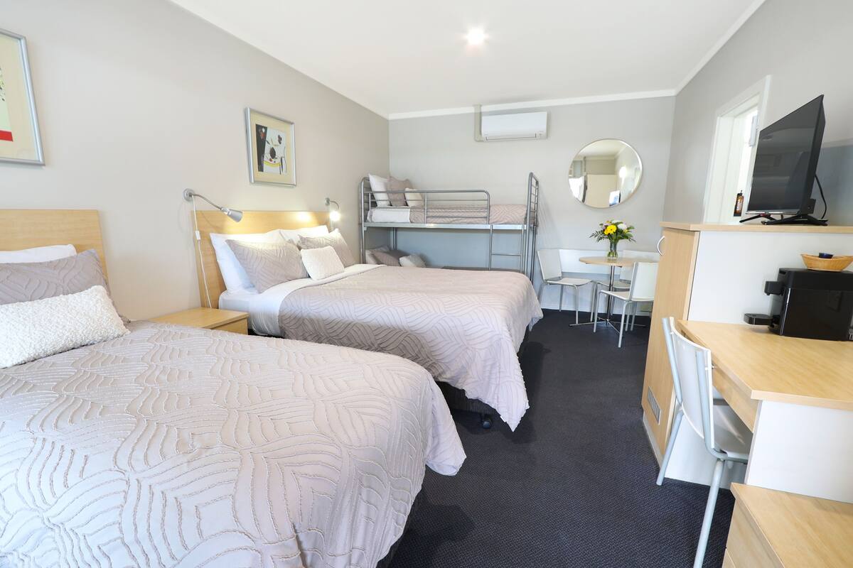 A hotel room with two beds, a desk, a chair, a television, and a small table with a vase of flowers.