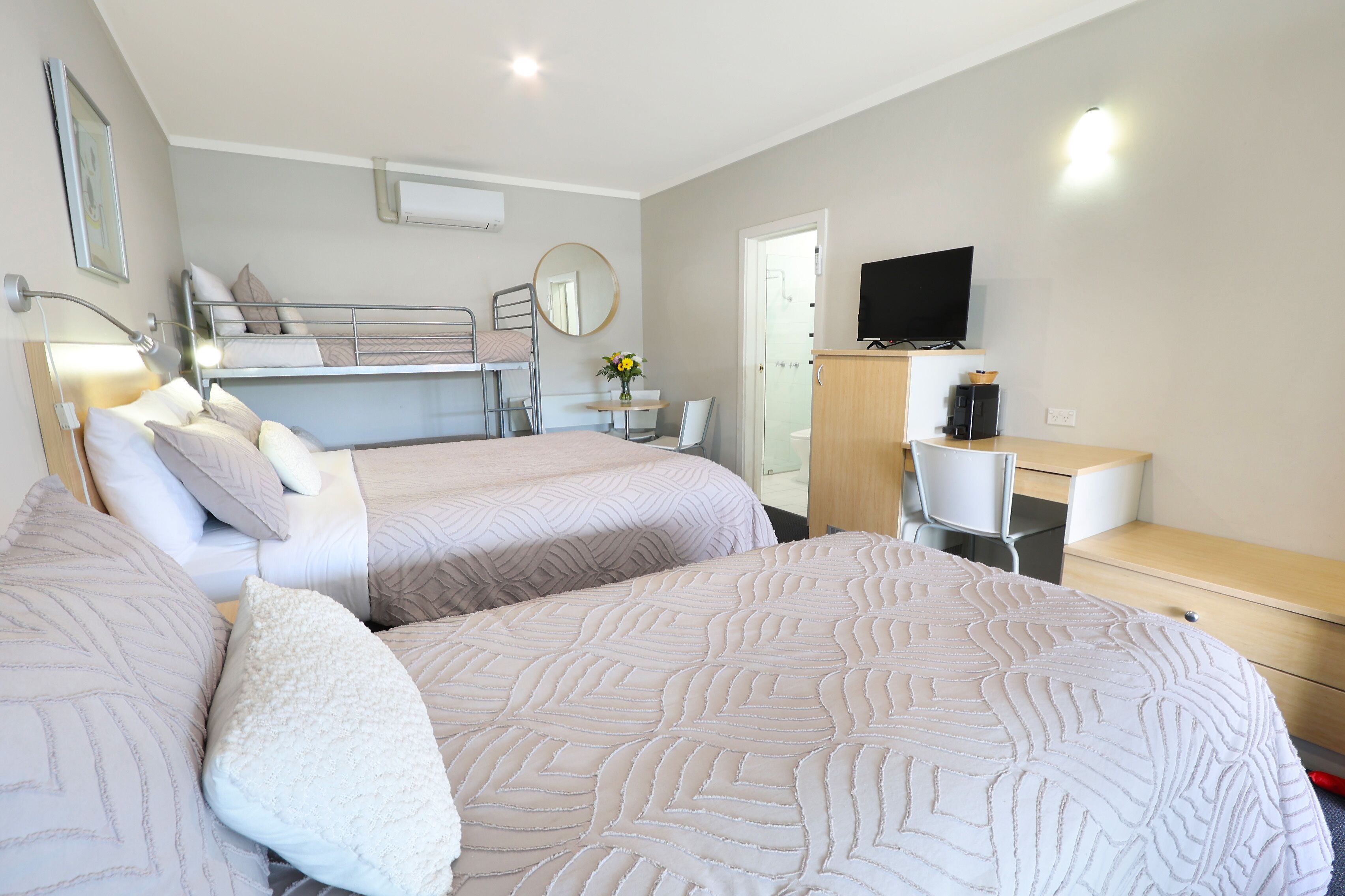 A hotel room with two beds, a desk, a chair, a TV, and a bathroom door.