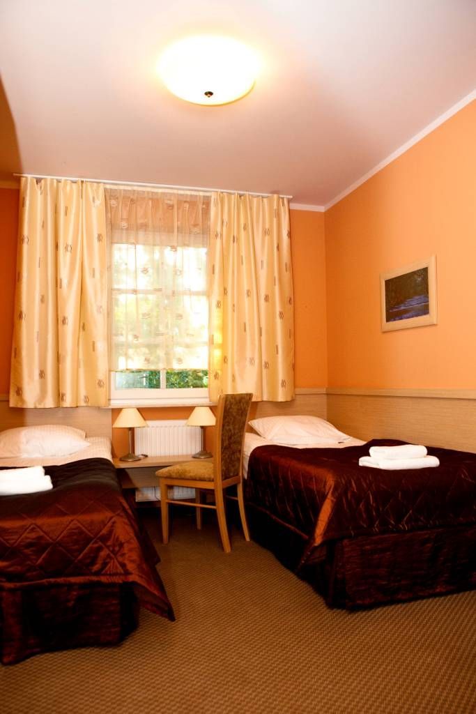 A hotel room with two beds, a desk, a chair, and a window with curtains.