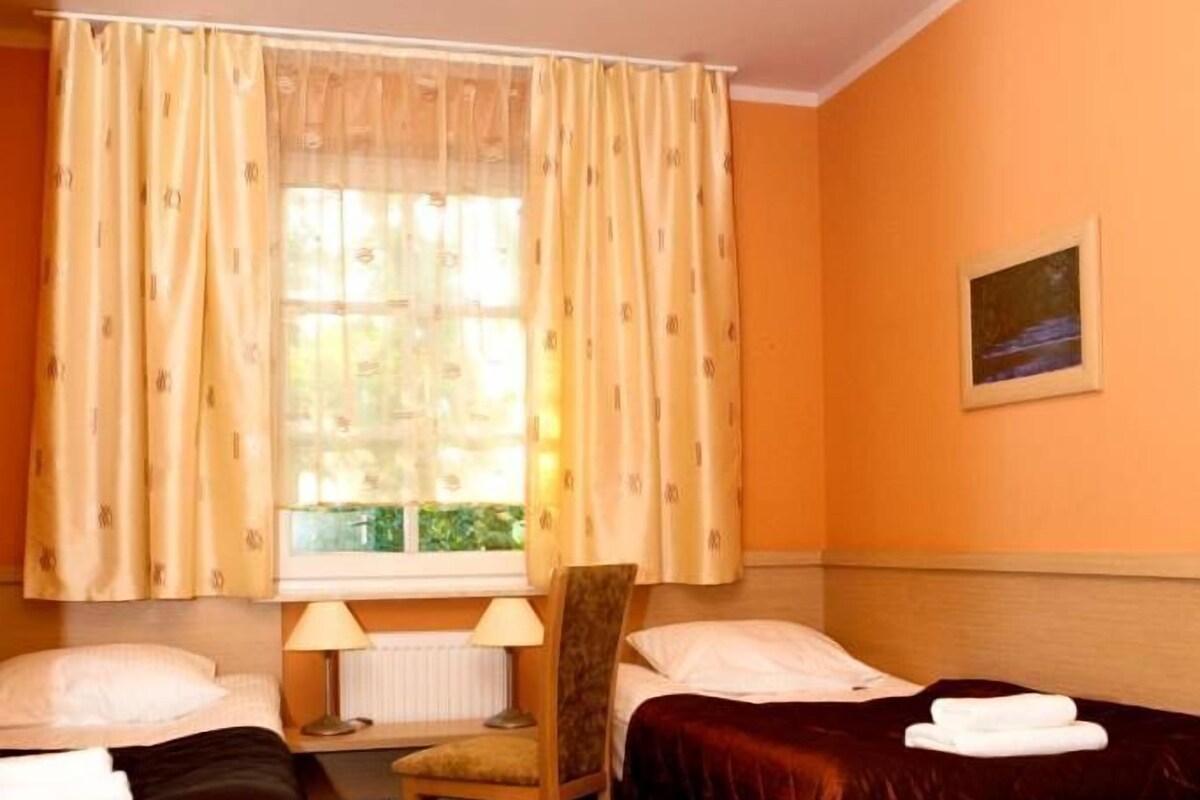 A hotel room with two beds, a chair, a desk, and a window with curtains.