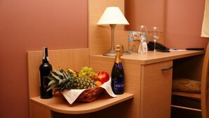 A minibar with a bottle of wine, a bottle of champagne, a fruit basket, and two glasses on a wooden counter. - Hotel Carskie Koszary (Zamosc)