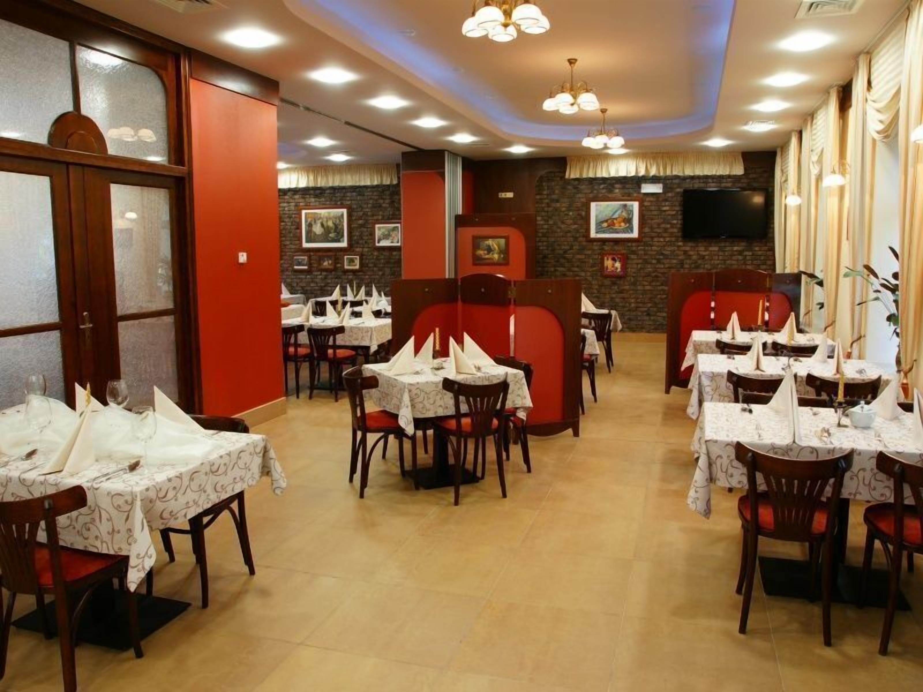A restaurant with multiple tables and chairs, some with white tablecloths and napkins.