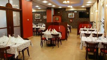 A restaurant with multiple tables and chairs, some with white tablecloths and napkins.