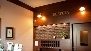 A reception desk with a wooden finish, a brick wall backdrop, and a sign that reads "RECEPTION". - Hotel Carskie Koszary (Zamosc)