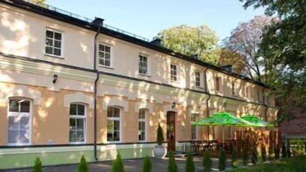 A two-story building with a green awning and a row of small trees in front. - Hotel Carskie Koszary (Zamosc)