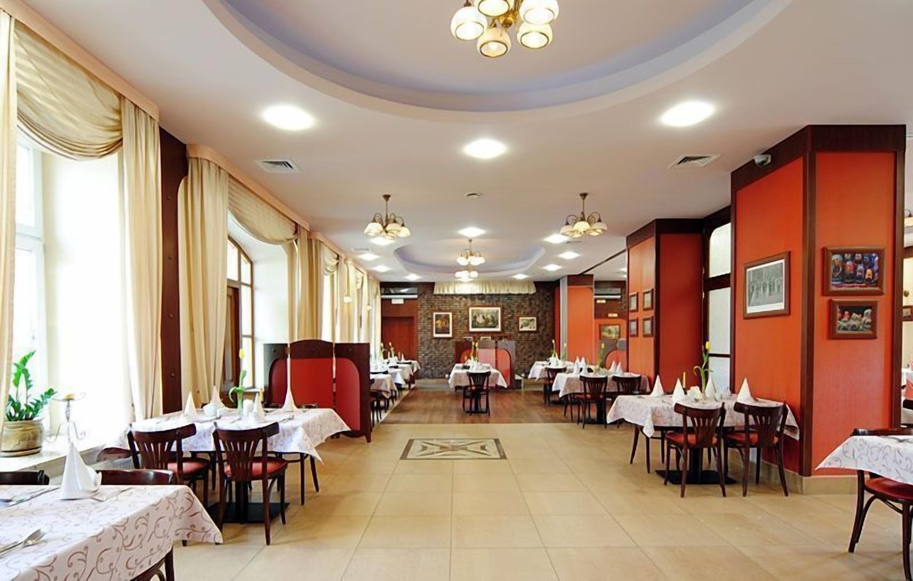A spacious restaurant with multiple dining tables and chairs, a central walkway, and a mix of red and beige walls.