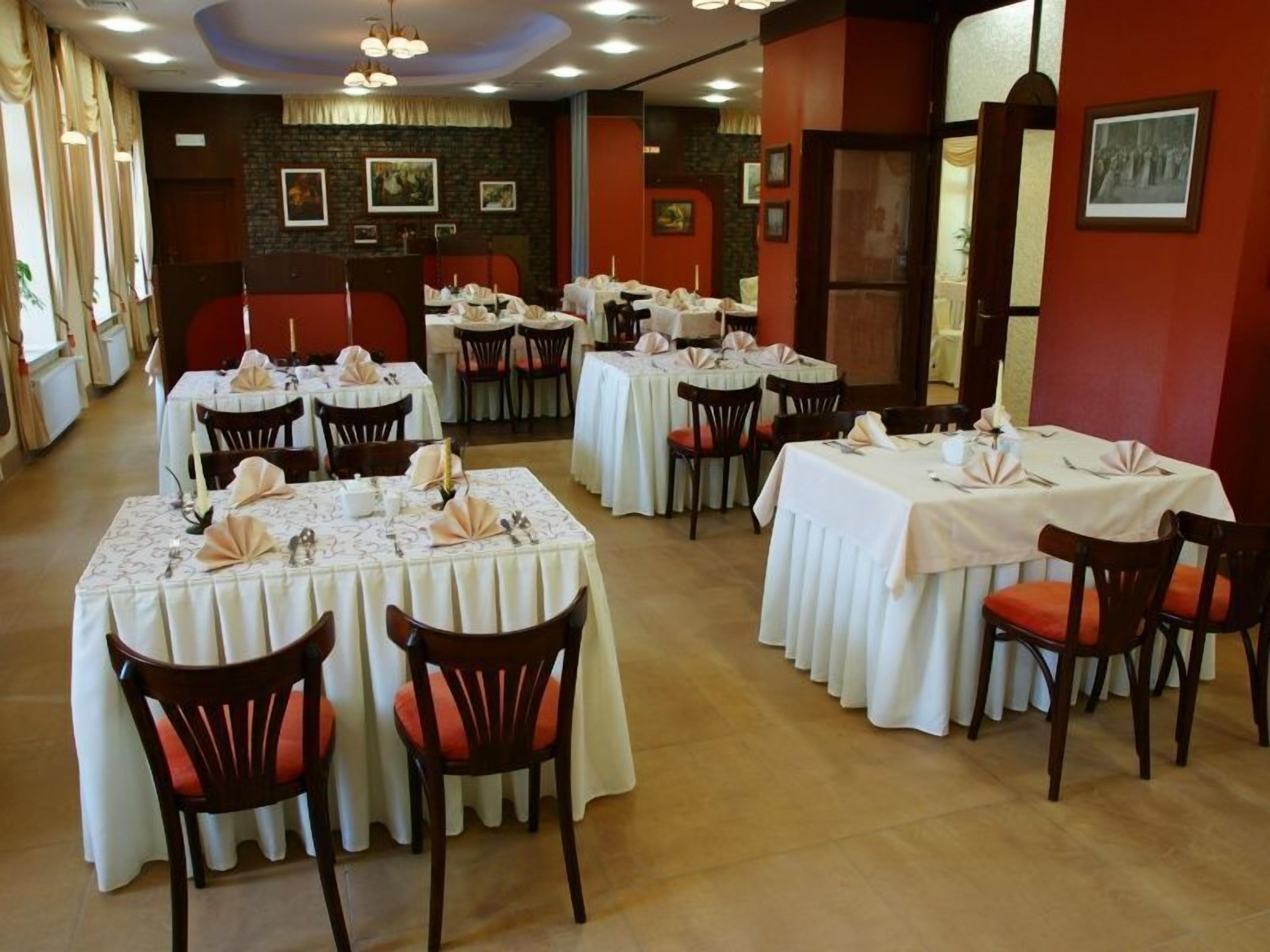 A restaurant with multiple tables set for dining, featuring white tablecloths and red cushioned chairs.