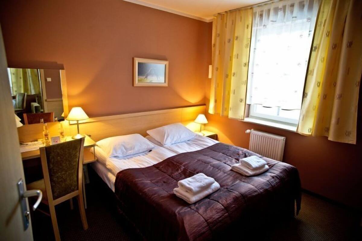 Une chambre d’hôtel avec deux lits, un bureau, une chaise et une fenêtre avec des rideaux.