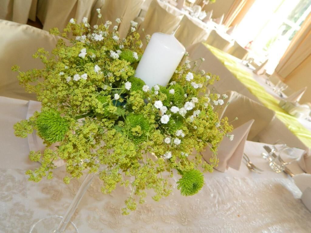 Una mesa servida con un centro de mesa floral, una vela blanca y un mantel.