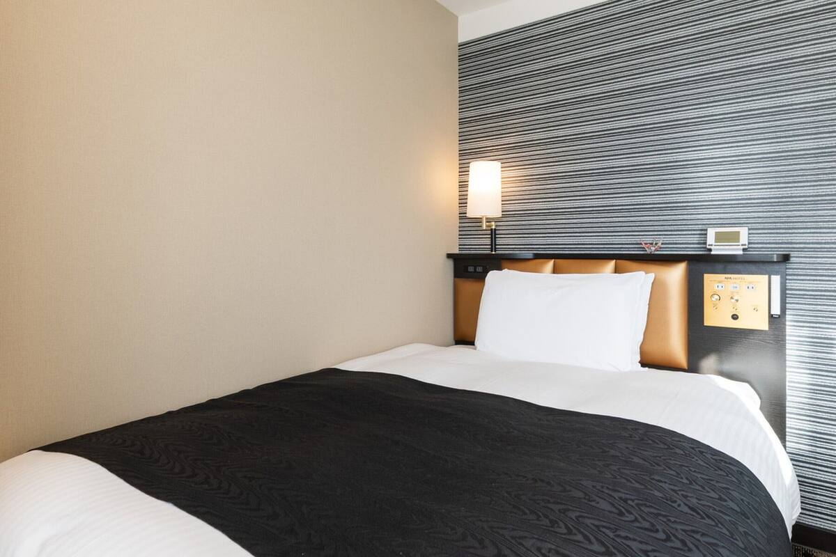 A hotel room with a bed, a headboard, a wall-mounted lamp, and a control panel.