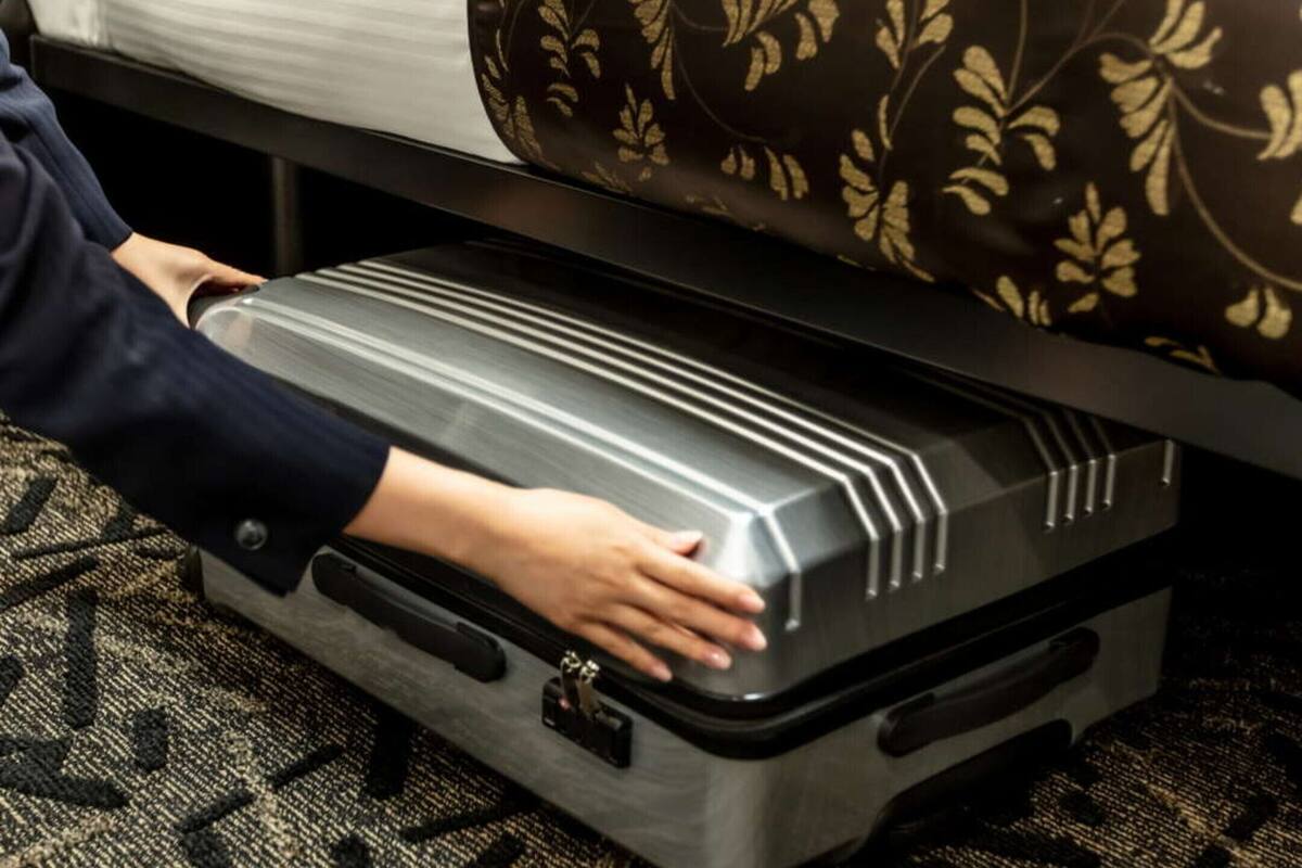 A suitcase being placed on a bed with a patterned bedspread.