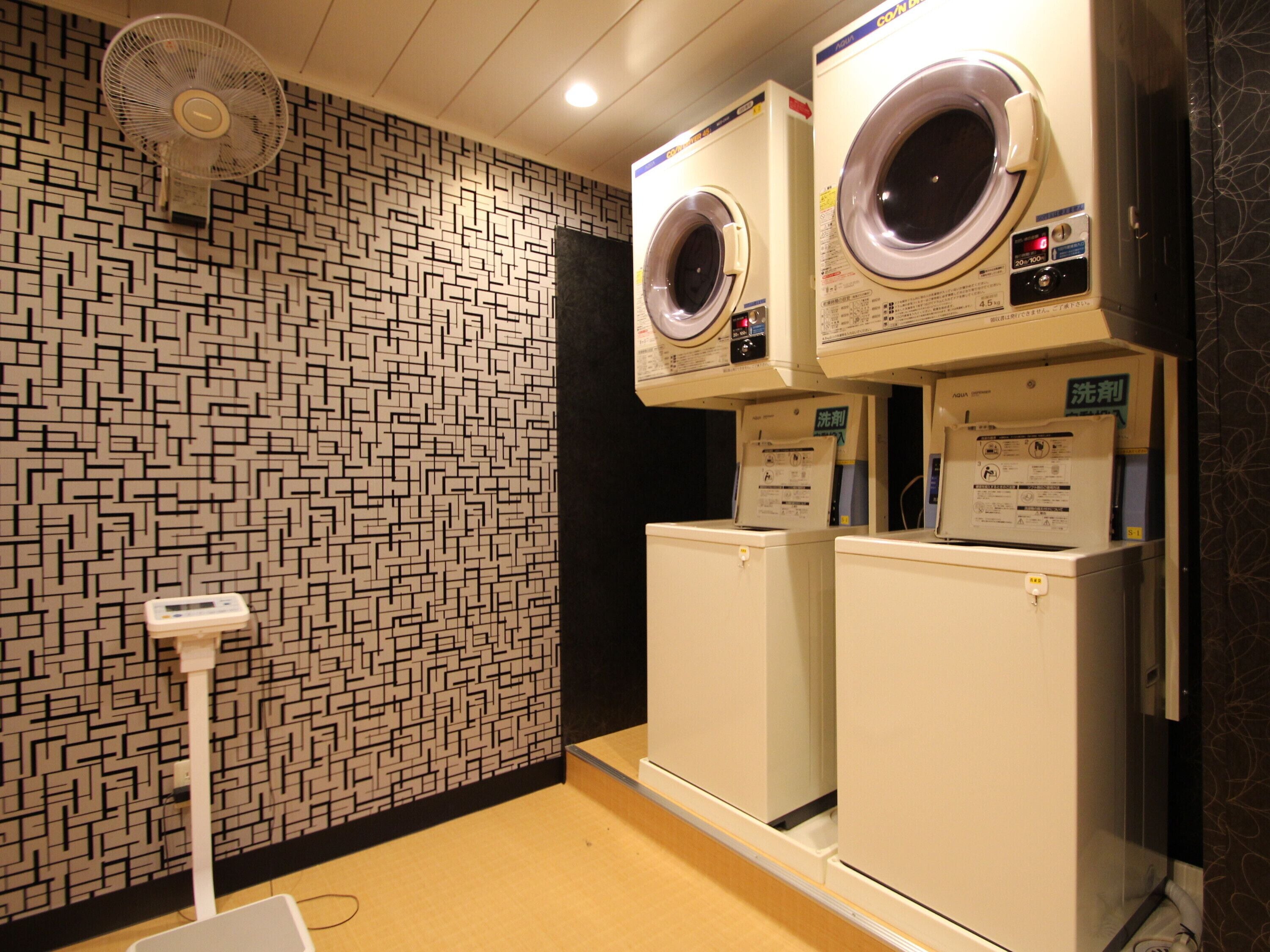 A laundry room with two stacked washing machines, a floor fan, and a patterned wall.