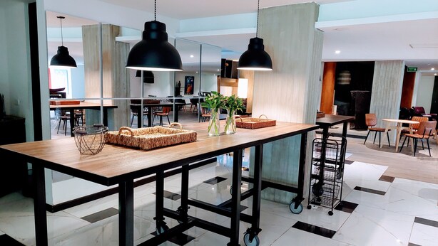 A modern dining area with a wooden table, black pendant lights, and a glass partition. - Viaggio Urbano (Bogotá)